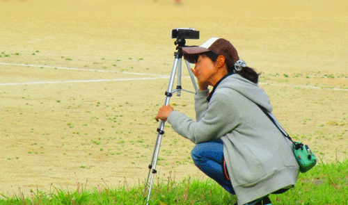 運動会でビデオを撮る帽子をかぶった女性の画像